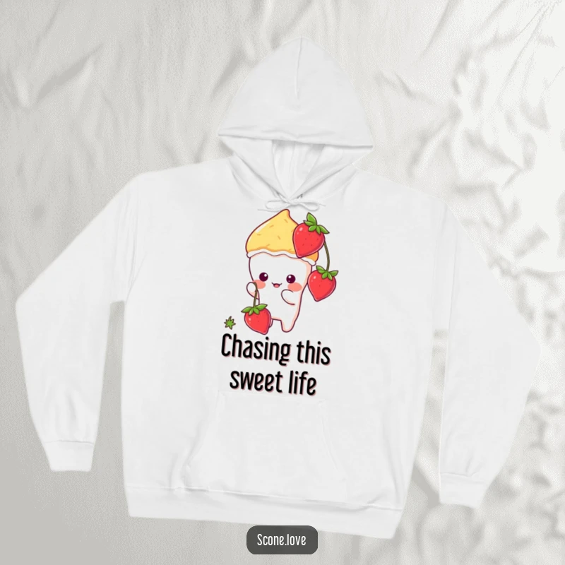 Funny animated kawaii scone character playfully batting at a dangling strawberry, featured on a warm, cozy hoodie.