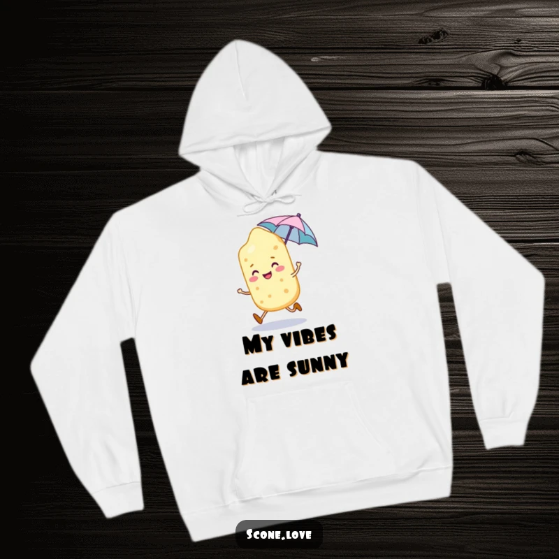 Funny smiling scone character skips joyfully, holding a tiny umbrella, featured on this cozy hoodie.